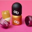 Un sistema de empaque de humectante labial recargable/reutilizable de arriba y más allá incluye una caja metálica en forma de cúpula y repuestos de productos empacados en material de base biológica.
