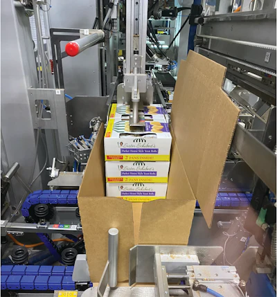 Seis cajas en dos pilas de tres se introducen en la estación de carga de la encajadora envolvente. Luego, la caja se empuja en ángulo recto debajo de las barras plegables y las herramientas que se cierran alrededor de la parte superior para comprimir la solapa superior y cerrarla.