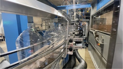 Botellas sopladas salen del equipo de moldeo por soplado a los transportadores Dyco.