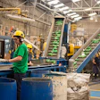 Industrial recycling facility with workers, blue barrels, and green conveyor systems