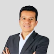 Smiling professional in dark suit and white shirt, standing with crossed arms