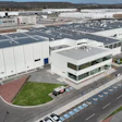 Aerial view of large white industrial manufacturing facility with parking lot and mountains