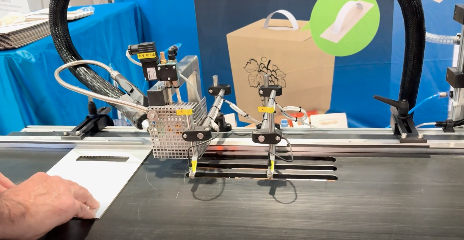 Sistema semiautom&aacute;tico de Allen Field para colocar manijas de papel, tela o bamb&uacute; reciclables en cajas plegadizas.