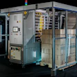 Industrial automation packaging machine with blue frame, control panels, and internal mechanical components visible through glass enclosure