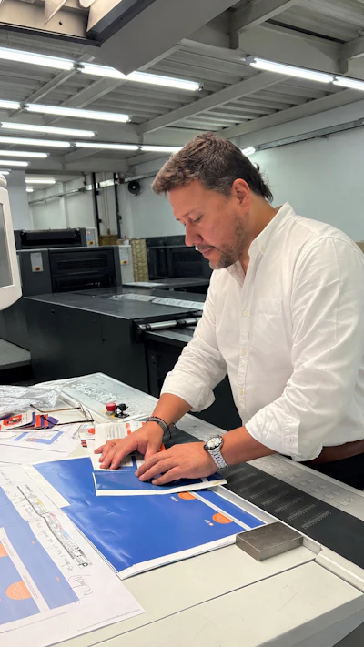 Man in white shirt reviewing blue printed materials at workstation in modern printing facility