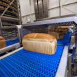 Fresh bread loaves on blue conveyor belt in industrial bakery production facility