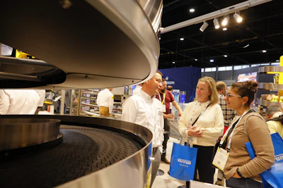 Professional attendees examine industrial equipment at a trade show exhibition with branded materials visible