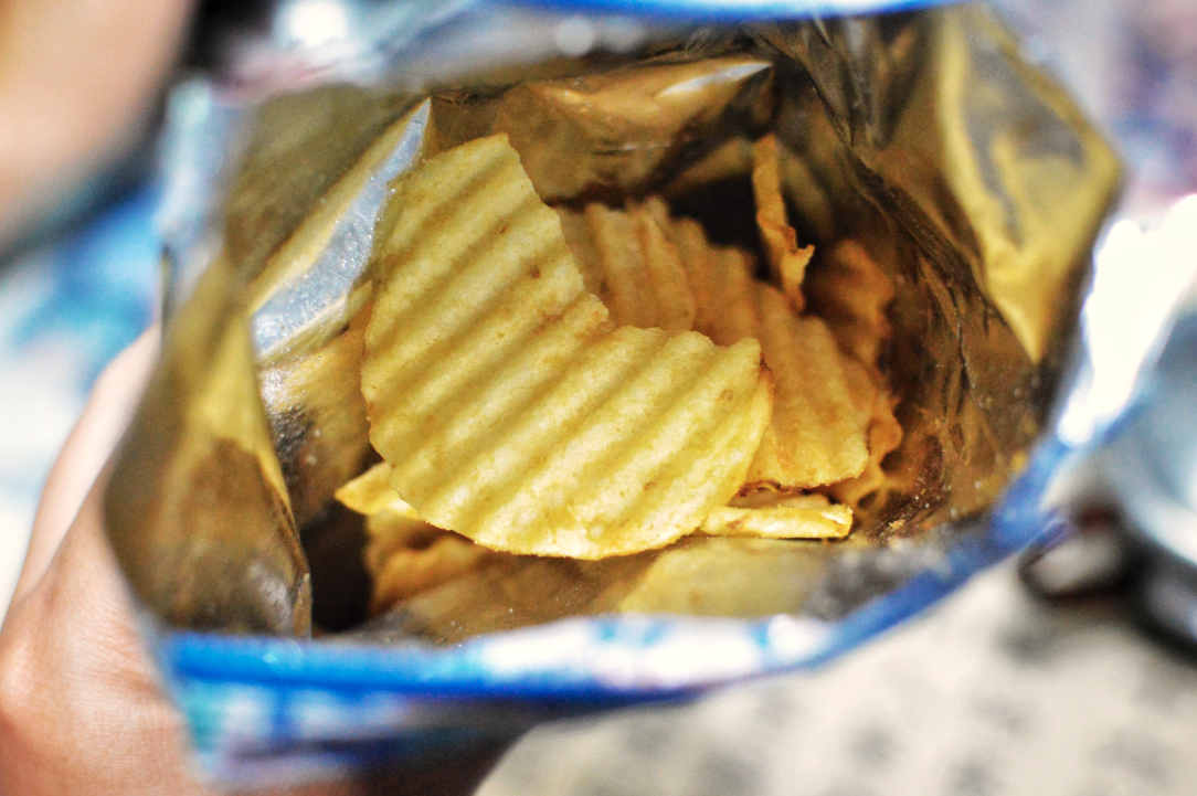 Open bag of ridged potato chips with golden-yellow wavy crisps visible inside blue and white packaging