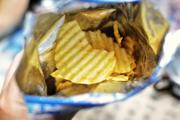 Open bag of ridged potato chips with golden-yellow wavy crisps visible inside blue and white packaging